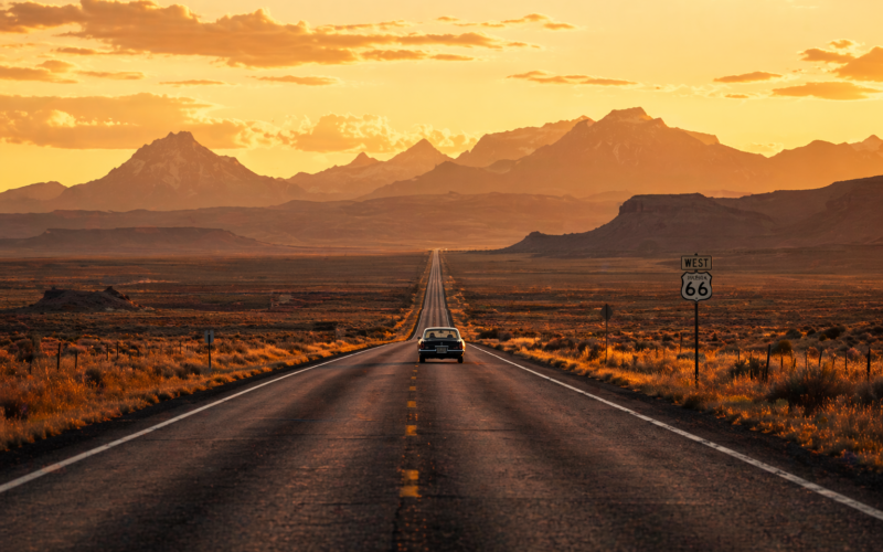 Scenic open road through the American West with mountains and golden sunset — best road trips USA